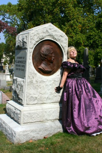 A dramatic pose by Marge Raymond at the grave of the producer of America's first musical.