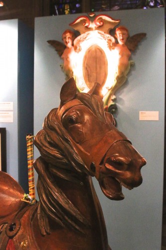 The Illions carousel horse, with its signature deeply-carved mane, and the Illions carousel decoration behind it.
