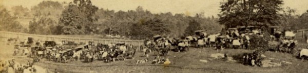 Detail of the above image, showing coaches, horses wearing blankets, and women sitting on grass, perhaps picnicking.